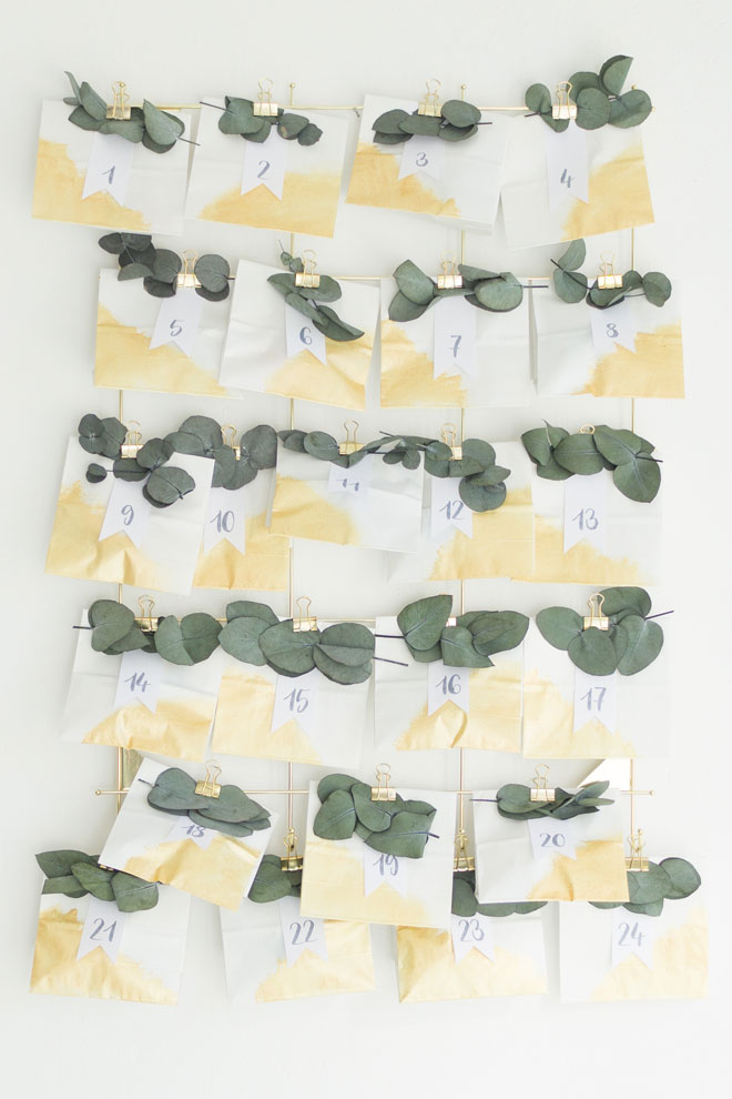 Adventskalender selber machen, DIY-Idee mit Eukalyptus und weiß-goldenen Papiertüten an der Wand angebracht