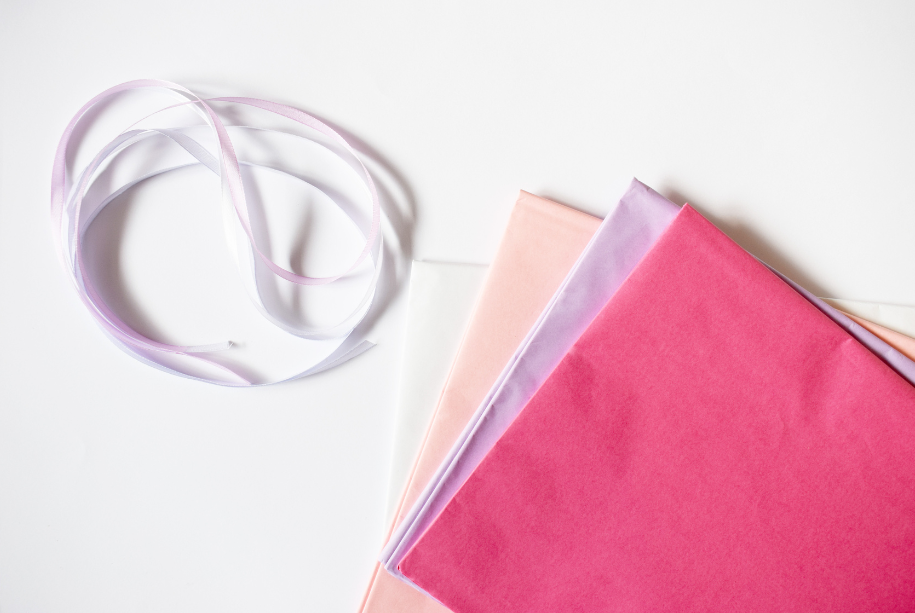 rosa und weißes Satinband neben je einem Bogen Seidenpapier in weiß, rosa, lila und pink