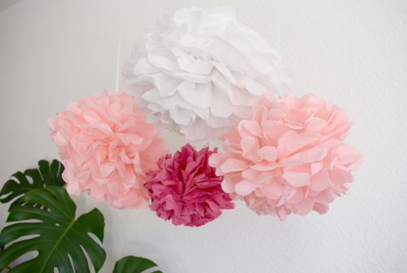 Rosa, weiße und pinke selbstgemachte Pompoms aus Papier hängend vor weißer Wand